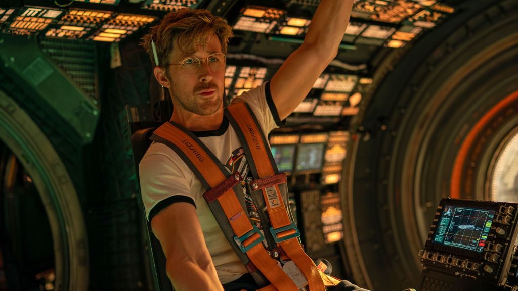 Ryan Gosling in a promotional still for the film is strapped in to a space pod wearing glasses and a pencil behind his ear and looking pensive.