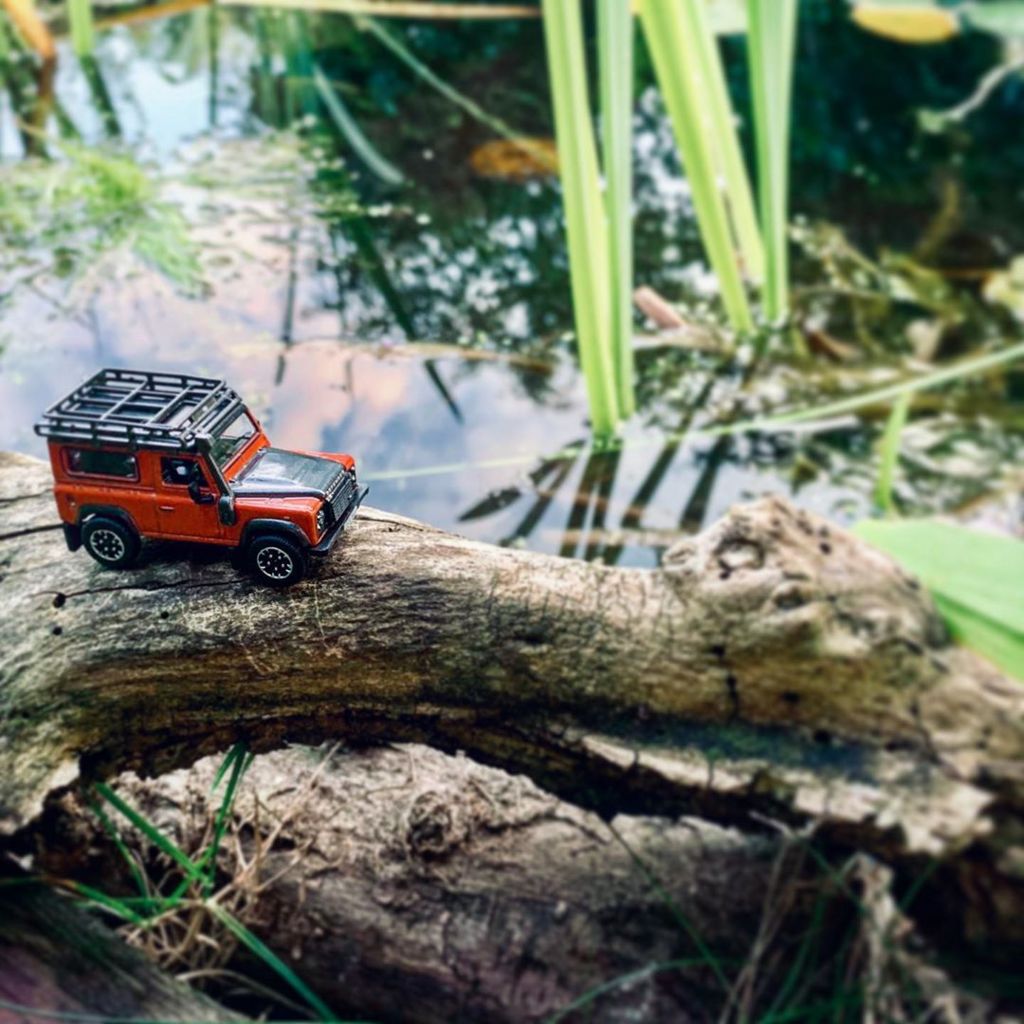 Red model Land Rover crosses water on a branch