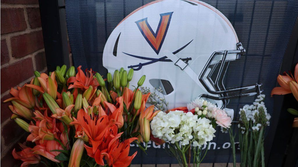 Flowers lay outside a memorial featuring an image of a University of Virginia football helmet