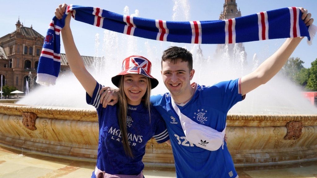 Rangers fans Dion Young and Callum Wilson hold a scarf aloft in front of a fountain in the Plaza de Espana