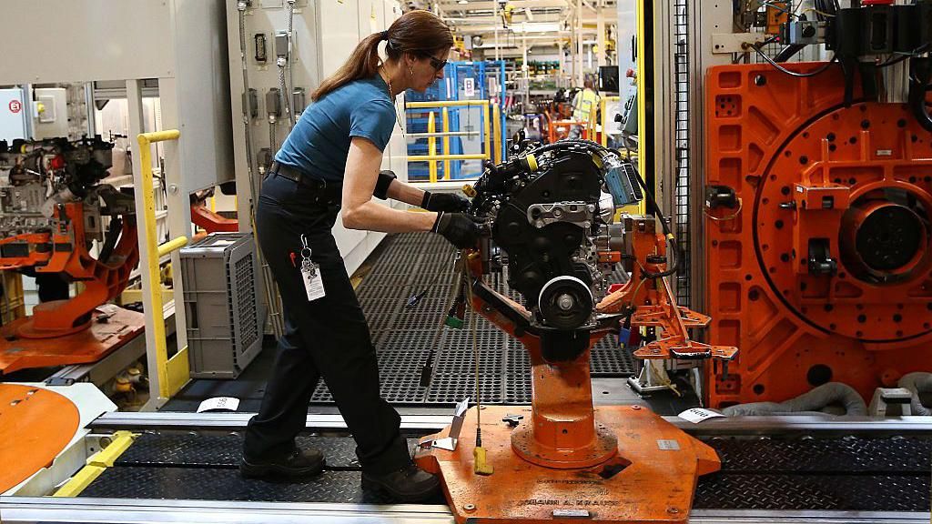 Woman works on black and orange machine in factory