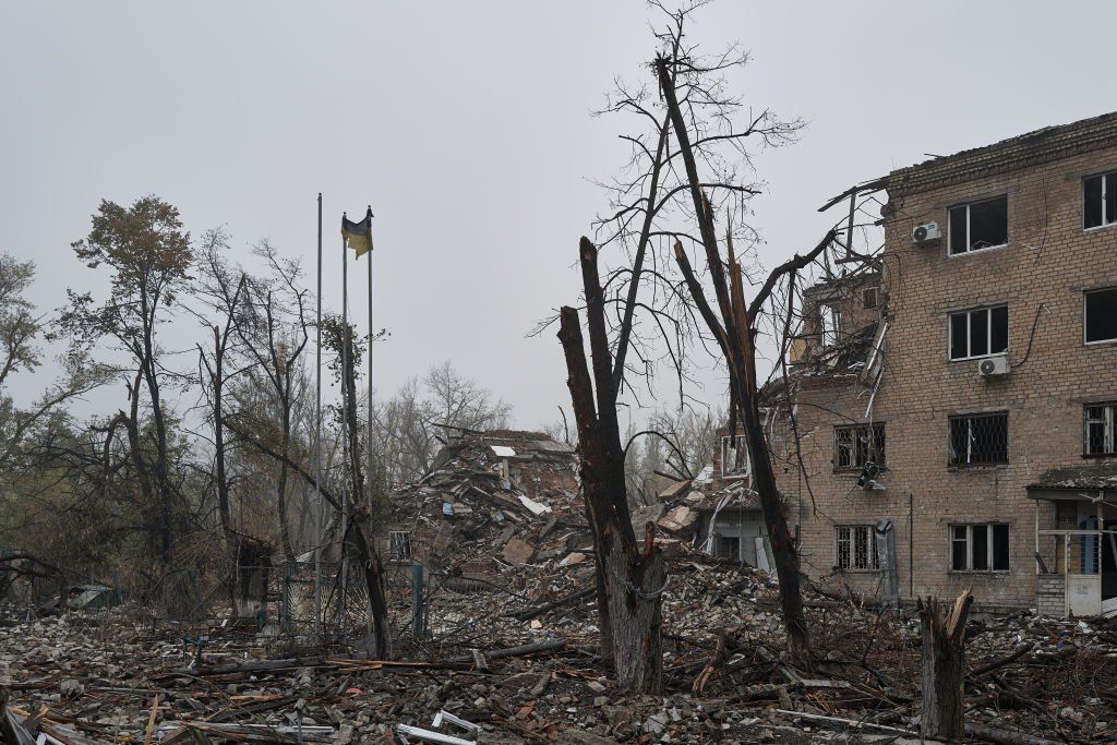 Обгоревшие деревья, одинокий украинский флаг и остатки разрушенного здания в Авдеевке, Украина