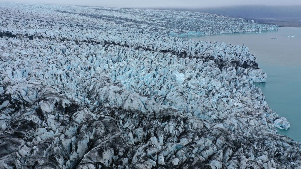 An aerial view of Breidamerkurjökull glacier, portions of it black with volcanic sand and stones, ends at Jökulsárlón lagoon