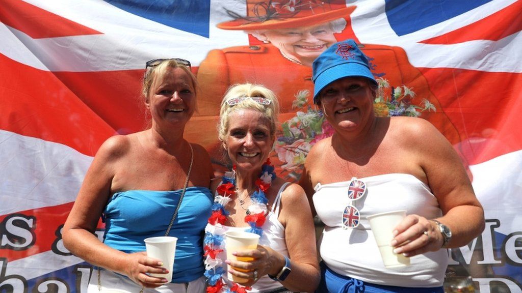 Three Rangers fans pose in front of a flag featuring the Queen
