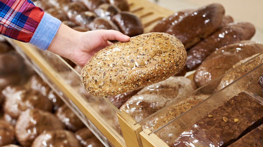A hand picks up bread from a shelf