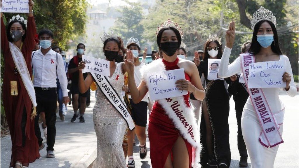 Участники конкурсов красоты демонстрируют салют тремя пальцами и держат плакаты, маршируя перед посольством США во время акции протеста против военного переворота в Янгоне, Мьянма, 10 февраля 2021 г.