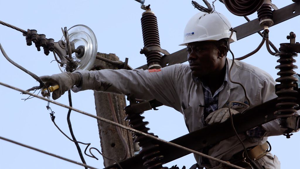 An engineer dressed in protective gear works on an electricity pylon