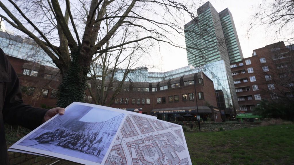 A woman's hand is just visible holding an old photo and map in which a tower block can be seen in the distance