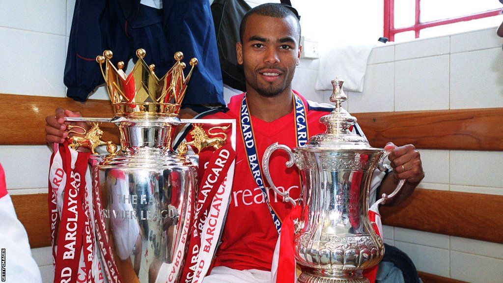 Ashley Cole posing with the Premier League and FA Cup trophies while at Arsenal