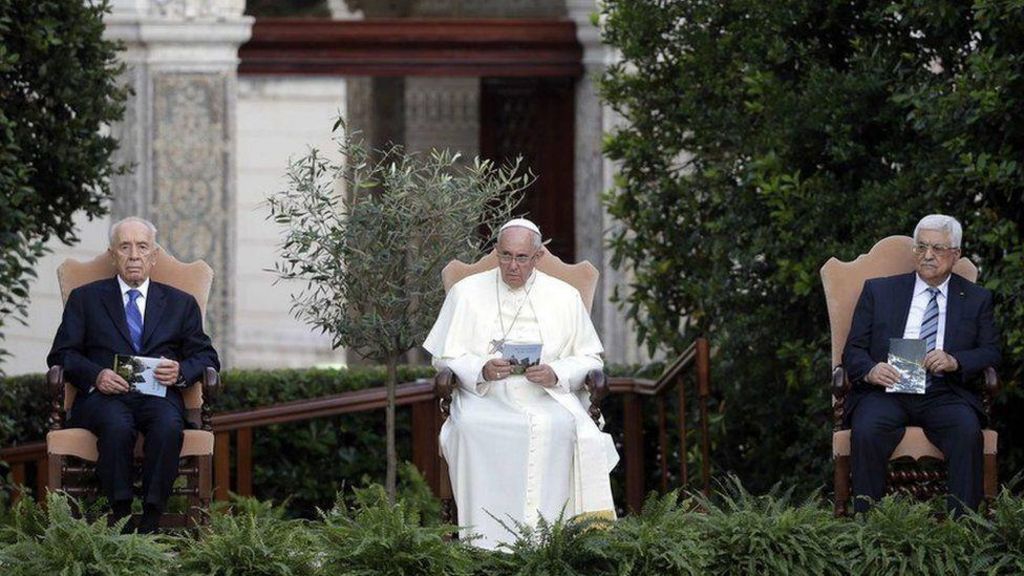 Pope Francis, Shimon Peres and Mahmoud Abbas. Pope Francis is in a garden with the two politicians flanking him. They are all seated.