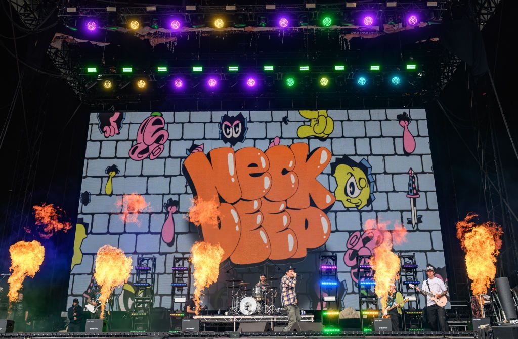 The five members of pop-punk band Neck Deep perform on the main stage at Leeds Festival. Fire comes out of the stage whilst they are stood in front of a colourful screen reading the name of the band.