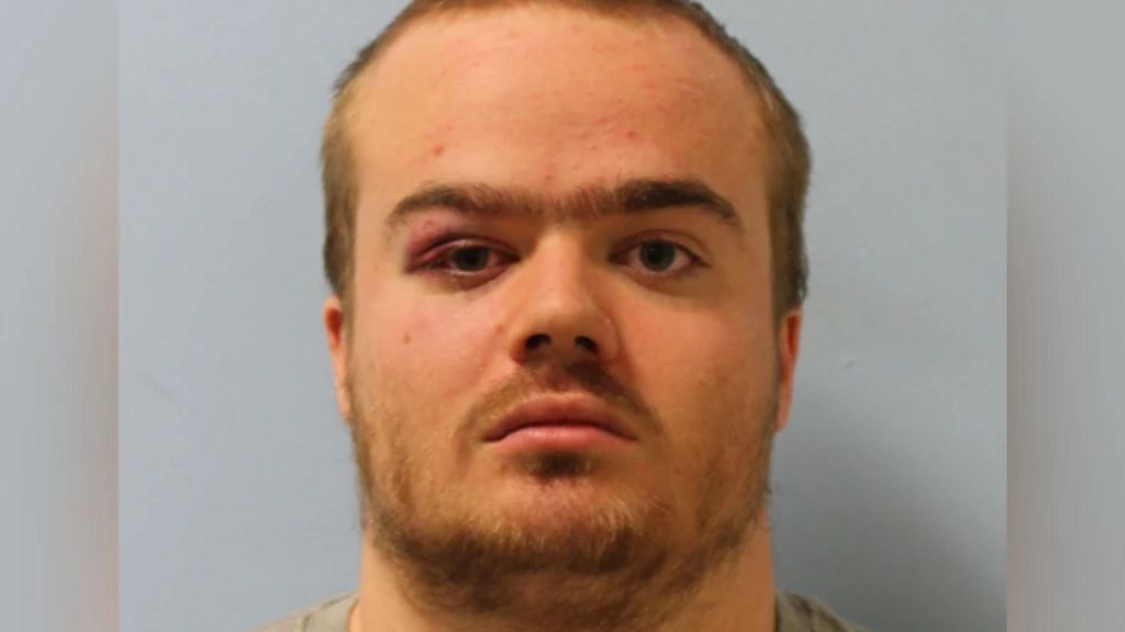 A mugshot of Jonty Bravery, who is wearing a grey shirt. He is staring at the camera and has a beard and short, blonde hair.