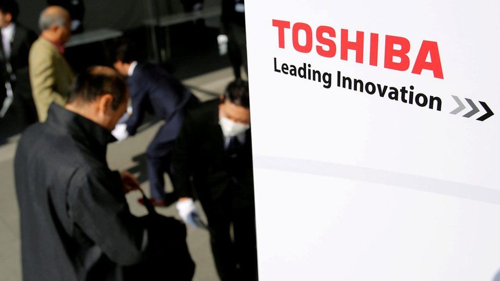 Businessmen stand beside a sign reading 'Toshiba - Leading Innovation'