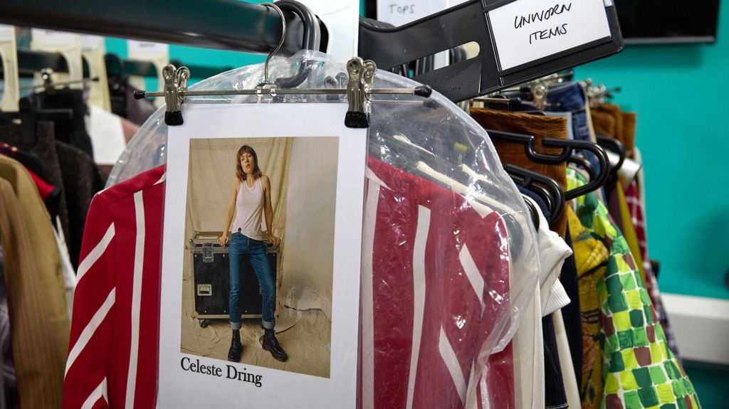 Various studio outfits for Celeste Dring hang on a clothing rail backstage.