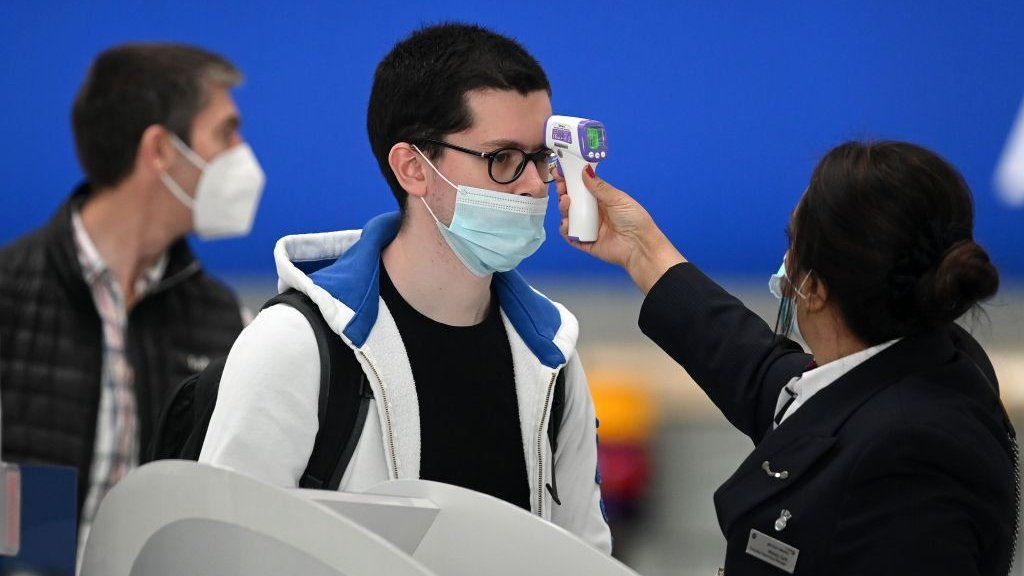Passengers wearing face masks or covering due to the Covid-19 pandemic, have their temperature taken as they queue at a British Airways check-in desk at Heathrow airport.