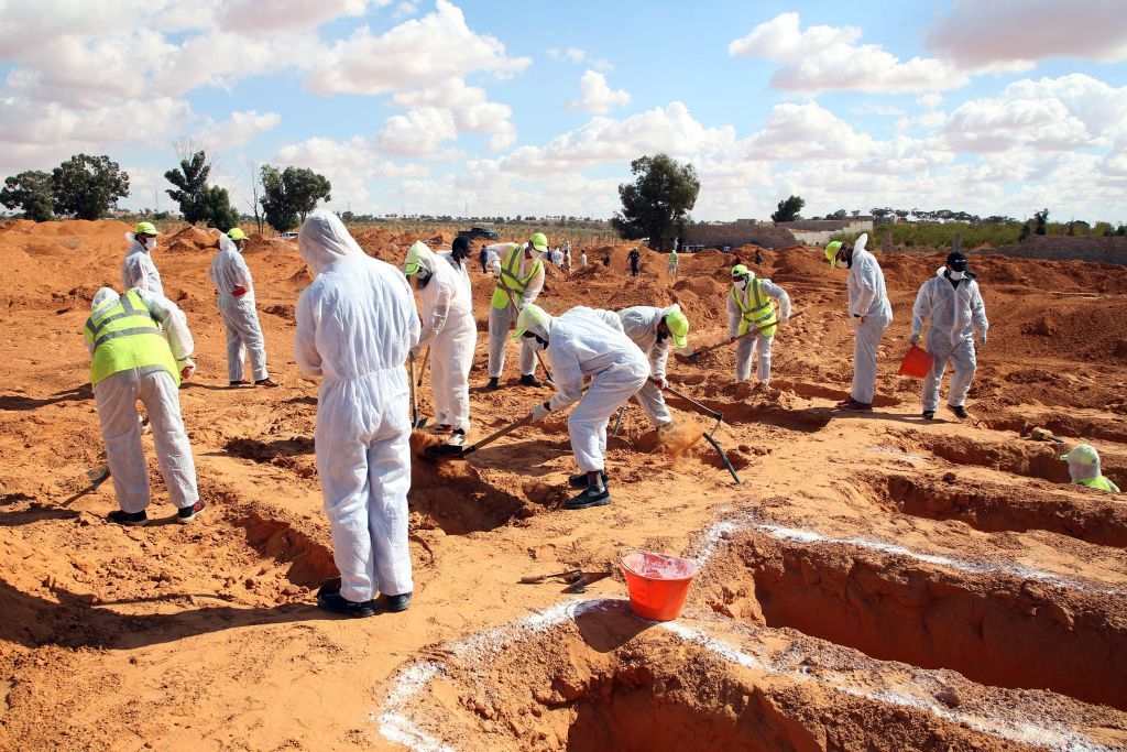 Men in white protection suits digging up bodies of the dead