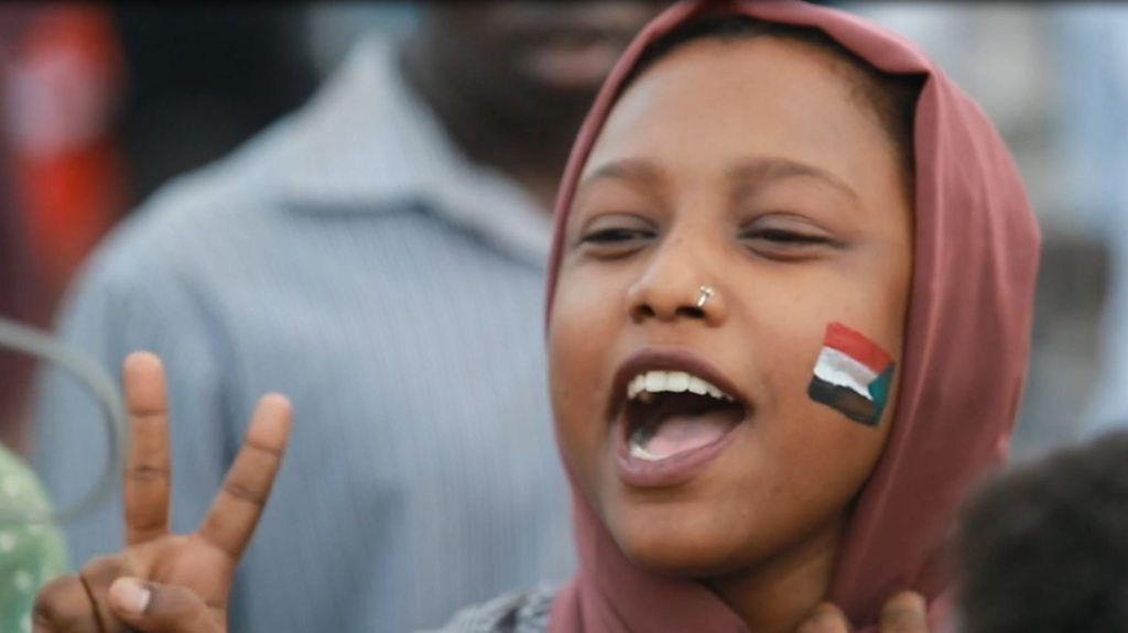 Female protester in Sudan with flag painted on her cheek
