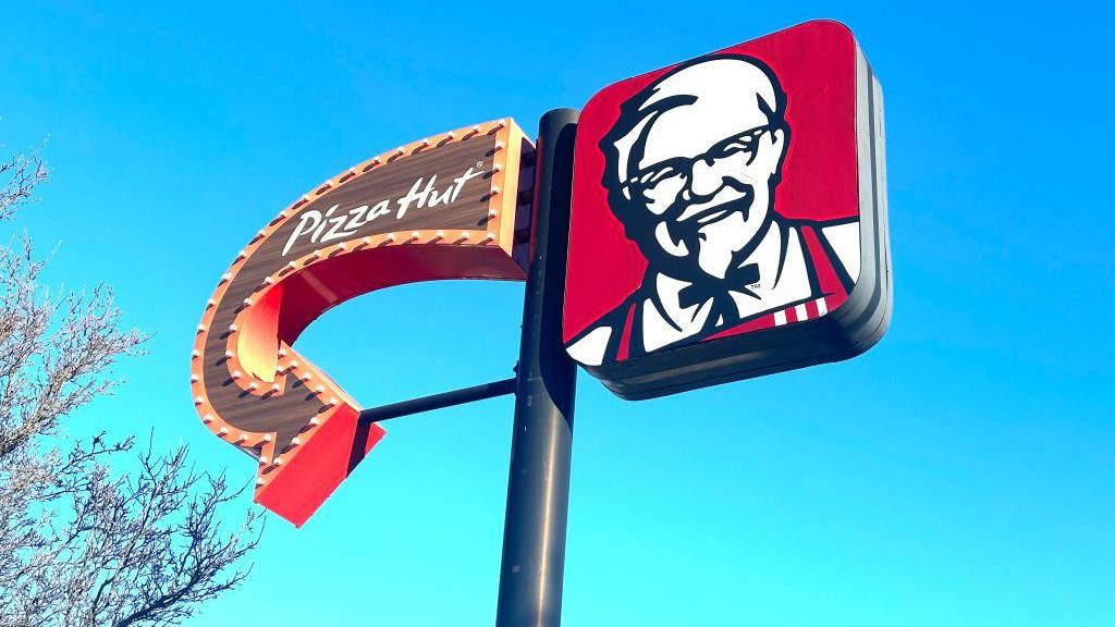 Sign with an arrow for Pizza Hut on the left and the KFC Colonel logo on the right