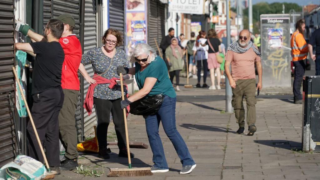 People clean up the streets with brooms following the protest