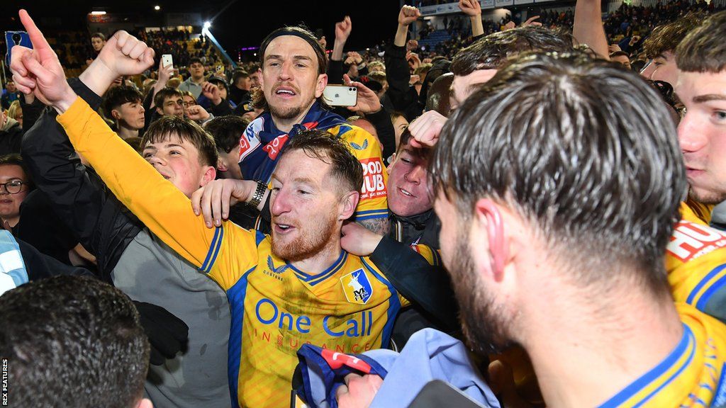 Stephen Quinn celebrates Mansfield Town's promotion among team-mates and fans on the pitch
