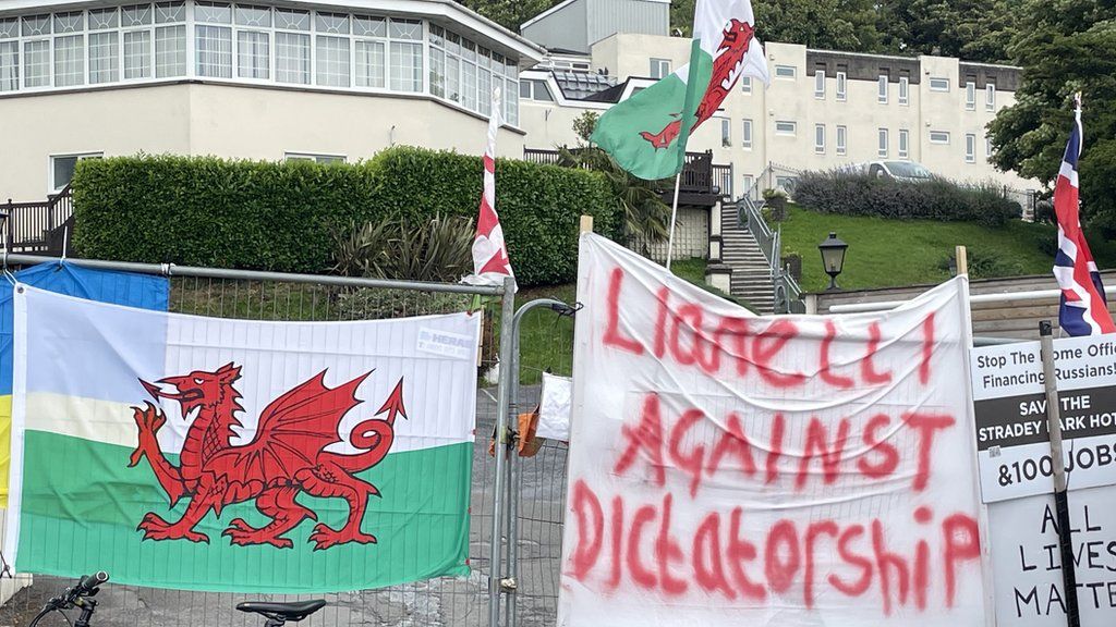 A Welsh flag and a message reading "Llanelli against dictatorship" hang on a metal fence erected in front of Stradey Park Hotel