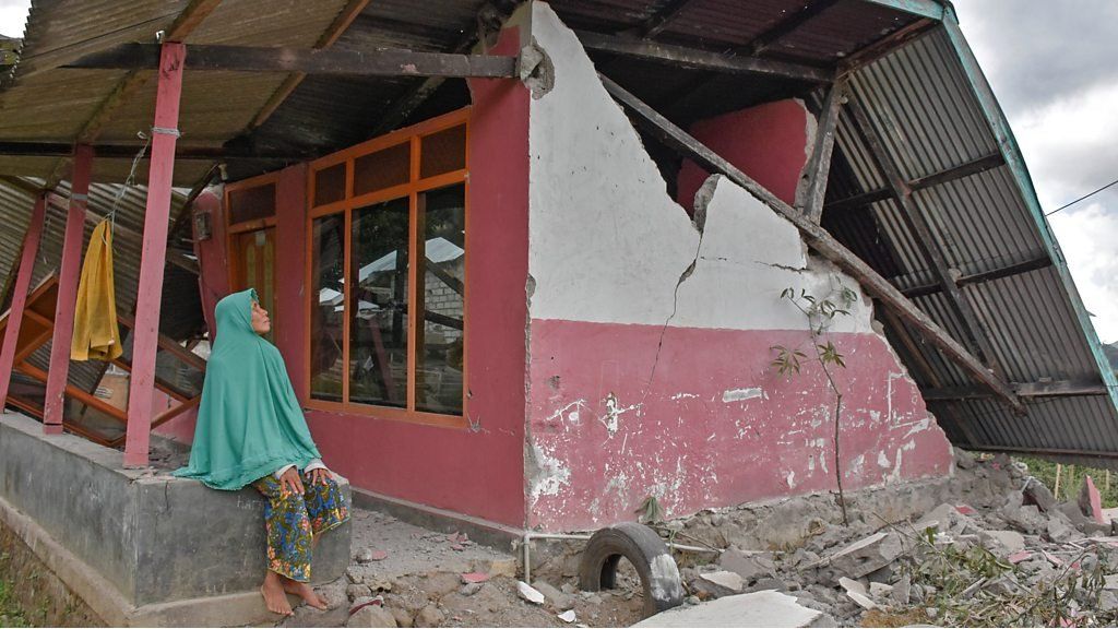 Woman sits outside a damaged house in Sembalun Bumbung village