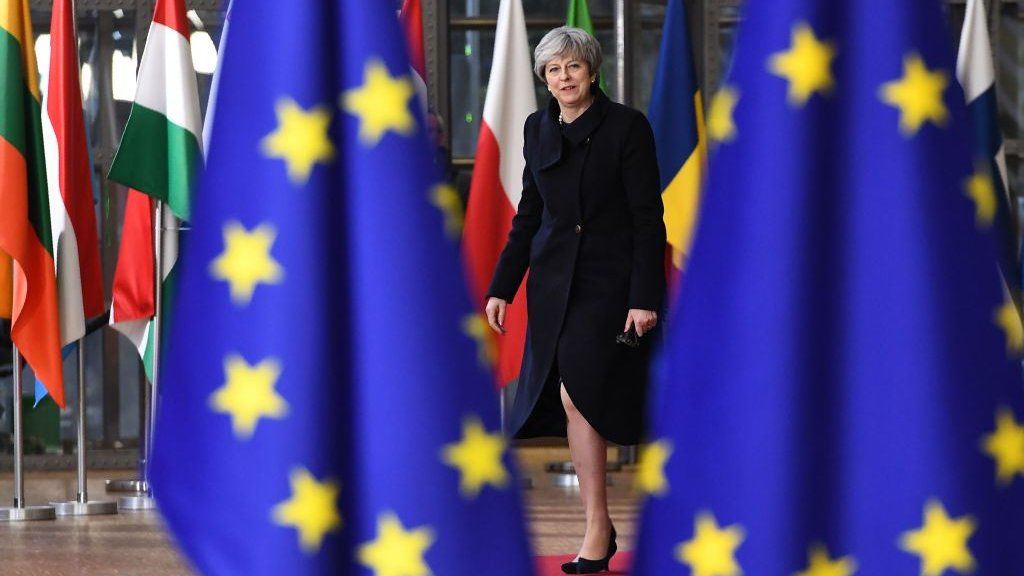 Theresa May standing between two EU flags