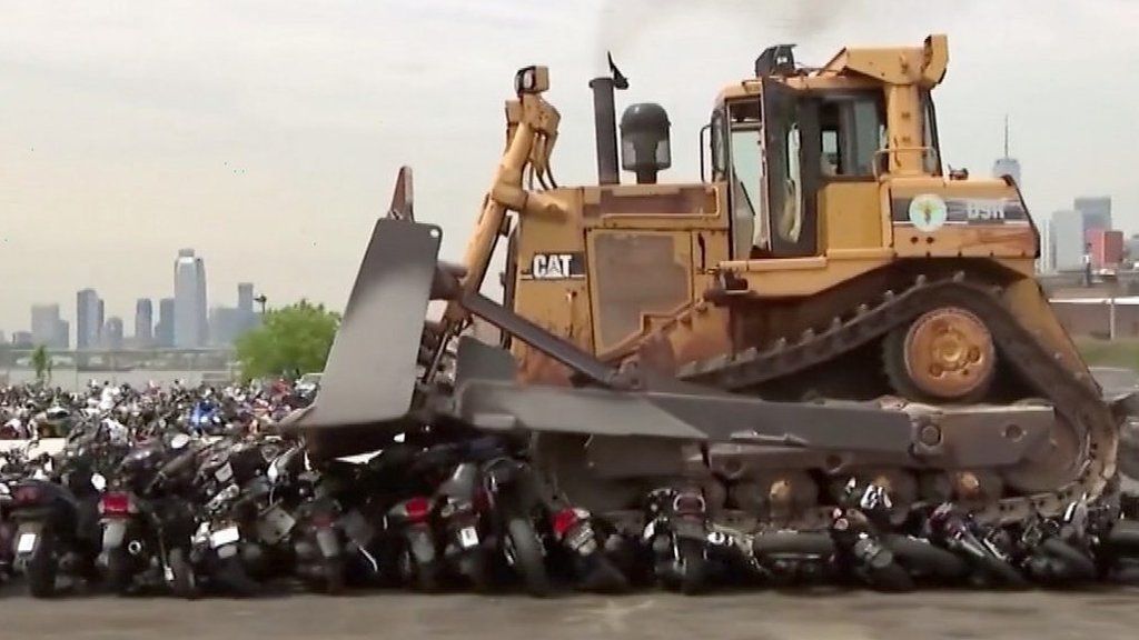 A bulldozer driving over dirt bikes and atvs