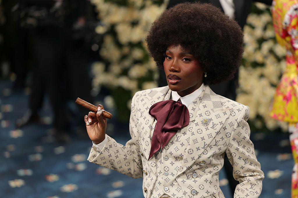 Doechii wears a custom smoking jacket, crimson cravatte and a cigar, while posing on the red carpet of the 2025 Met Gala