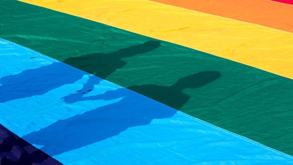 Shadow of two people holding hands cast on a rainbow flag