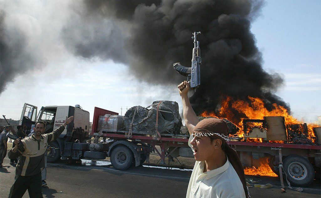 Iraqi Sunni Muslim insurgents in front of a burning US convoy on the outskirts of Fallujah, Iraq, 2004