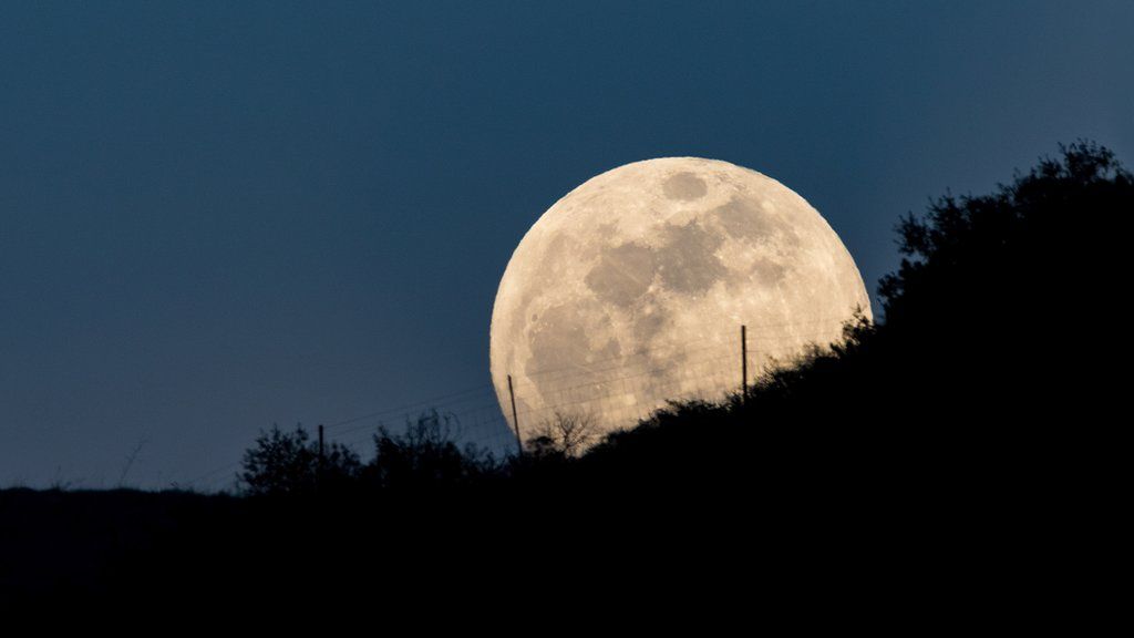 The Moon rising over a hill with a fence