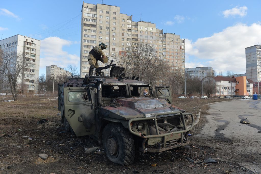 A Ukrainian territorial defence soldier examines a burnt-out Russian army vehicle in Kharkiv