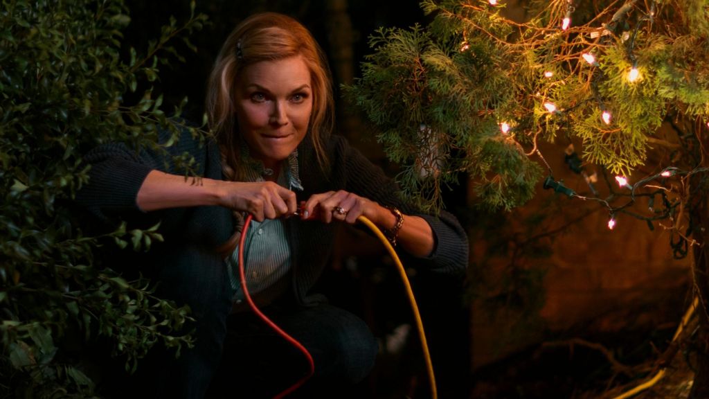 Michelle Pfeiffer holding two electric cables for Christmas lights and plugging them together with a mischievous look on her face