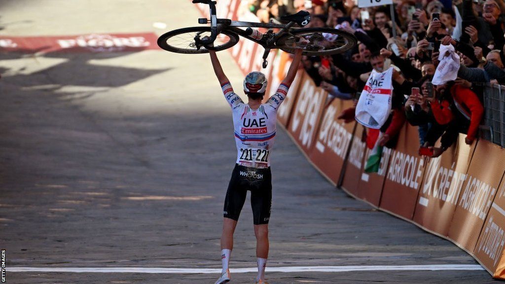 Tadej Pogacar lifts his bike above his head in front of spectators at the finish of the Strade Bianche