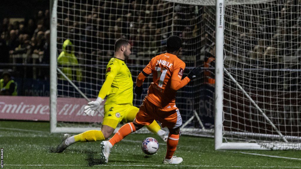 Blackpool's Karamoko Dembele scoring his side's second goal past Bromley's goalkeeper Grant Smith during the Emirates FA Cup First Round match between Bromley and Blackpool at Hayes Lane on November 4, 2023 in Bromley, England