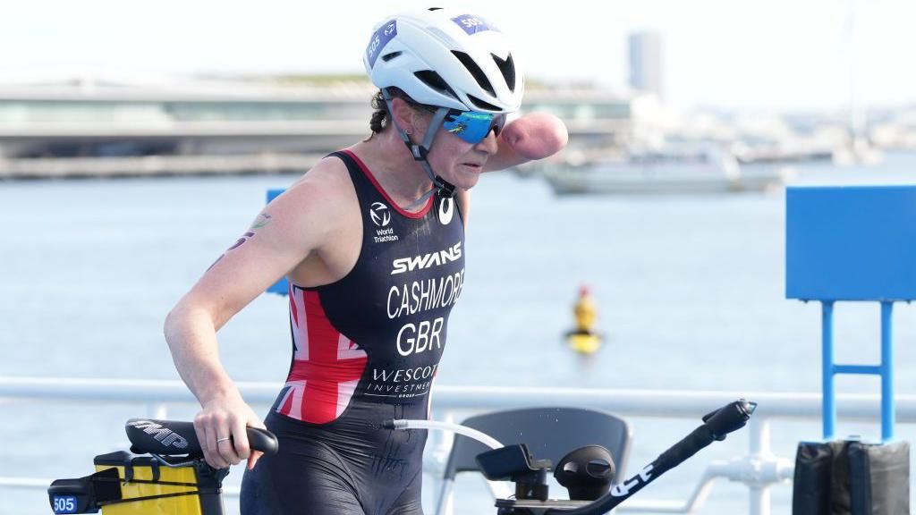 Claire Cashmore holding her bicycle while competing in a triathlon