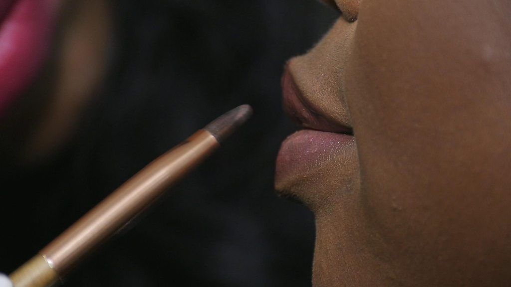 A makeup artist applies lip colour to a woman