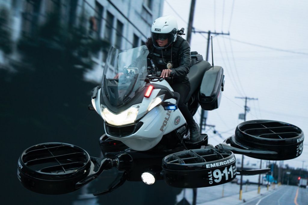 Kali Reis riding a futuristic police bike, which flies 