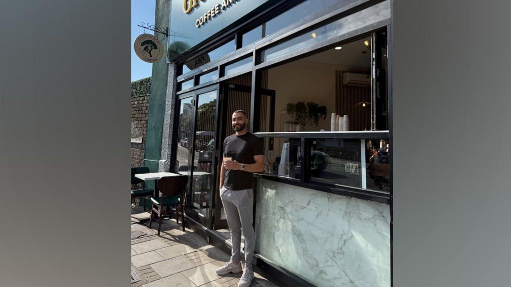 Rusty Nart leans against the entrance to his coffee shop, holding a coffee