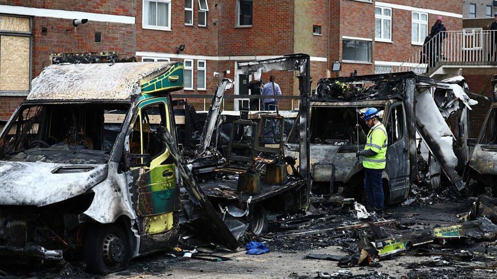 An official works among the burnt out ambulances at the scene of an antisemitic arson attack in the Golders Green neighbourhood of north London