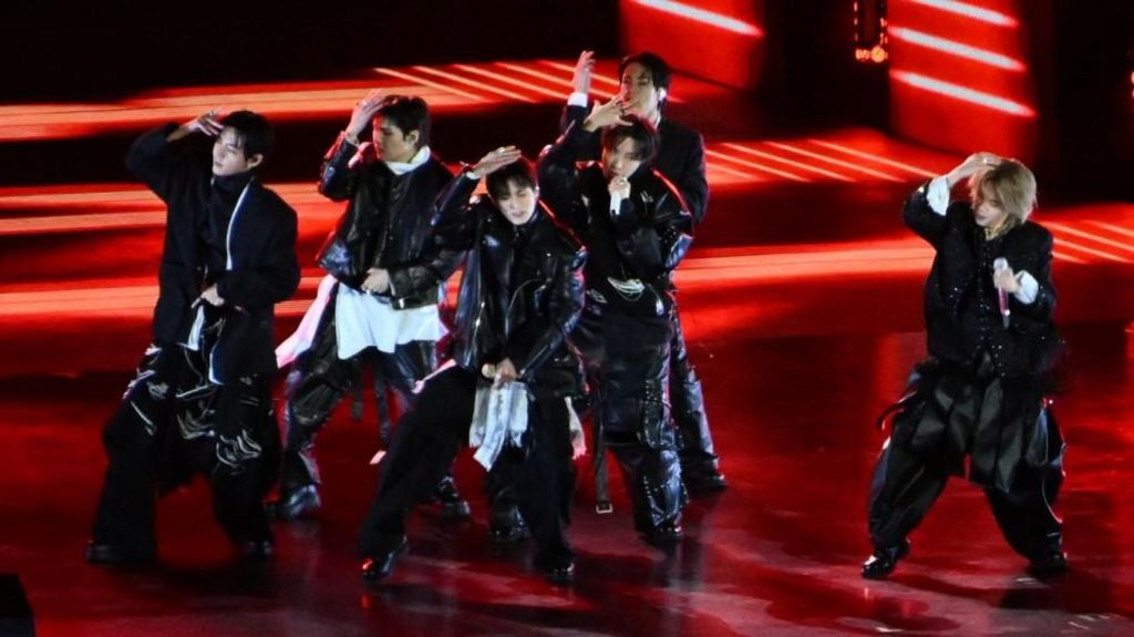 Wearing black and white and touching their heads, six of seven members of the K-pop group BTS performs on a red stage during the 'BTS THE COMEBACK LIVE | ARIRANG' concert