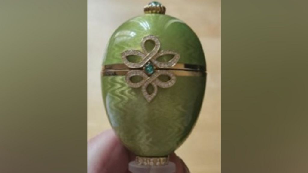 Close-up of a green Fabergé egg ornament featuring a gold band around the centre and a decorative diamond‑patterned design with a small blue‑green gemstone.
