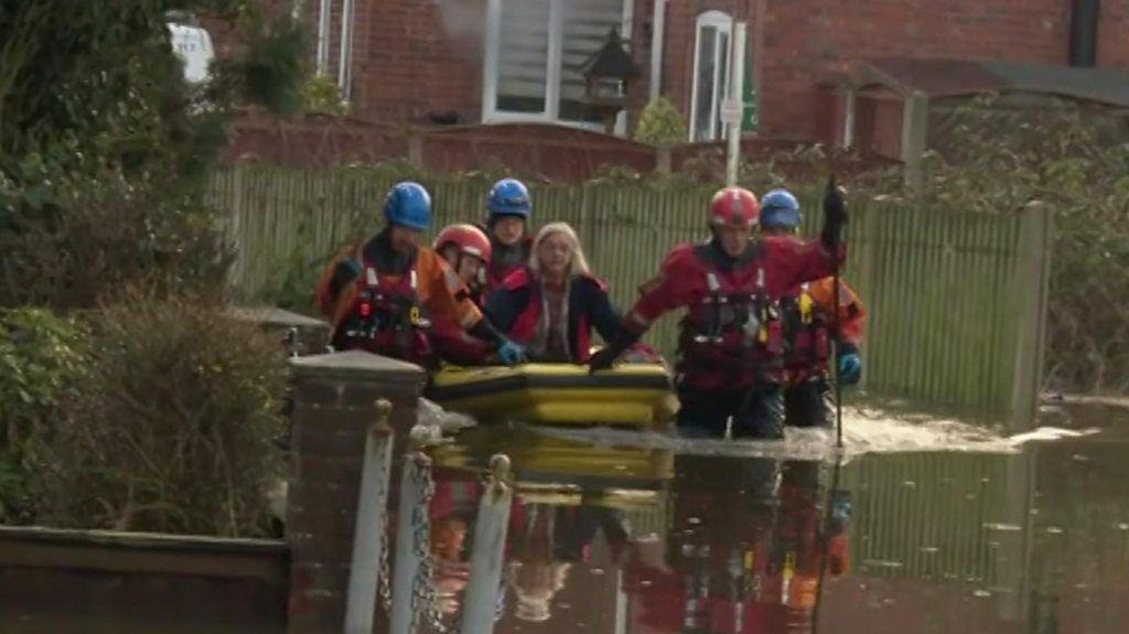 Rescuers guide a woman in a dinghy in flood water