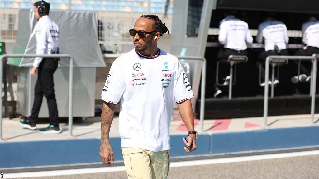 Lewis Hamilton walks in the Bahrain paddock with the Mercedes crew in the background