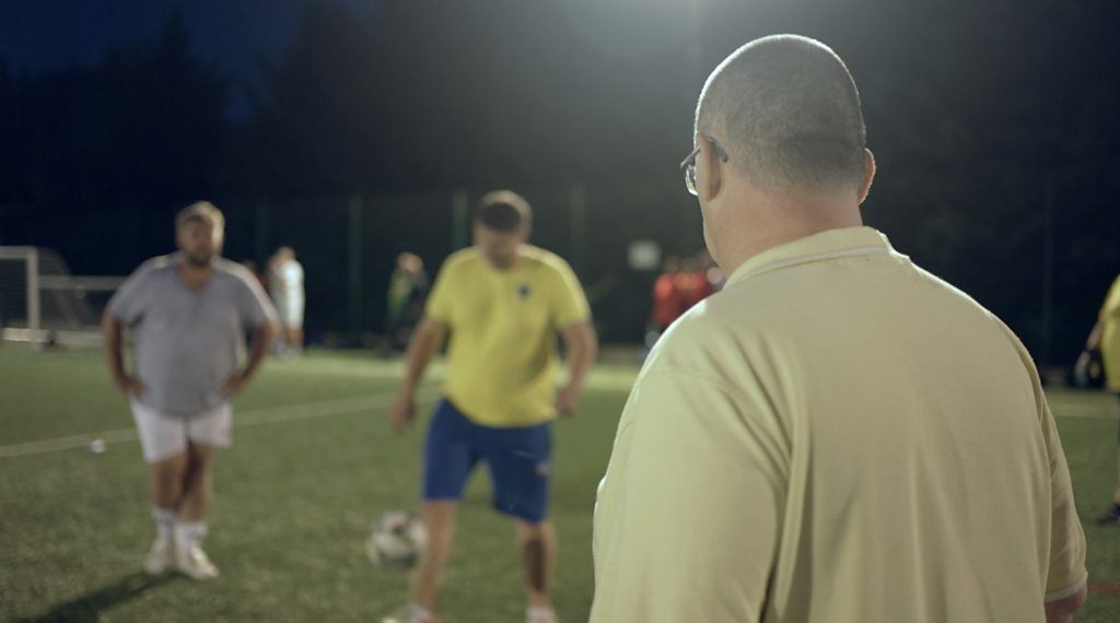 Man in foreground watching men blurred in the background playing football