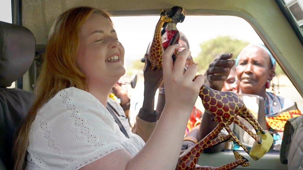 Maasai women try to sell dozens of wooden animals to Lucy when she arrives in their village