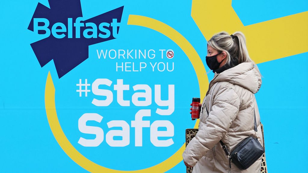 Woman walks past a 'stay safe' sign in Belfast