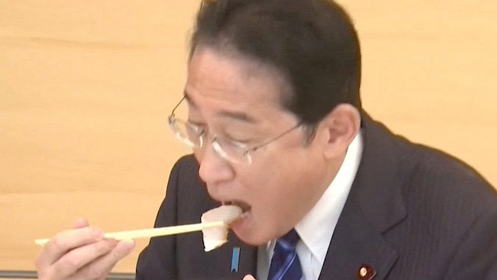 Japanese Prime Minister Fumio Kishida putting a piece of sashimi into his mouth using chopsticks