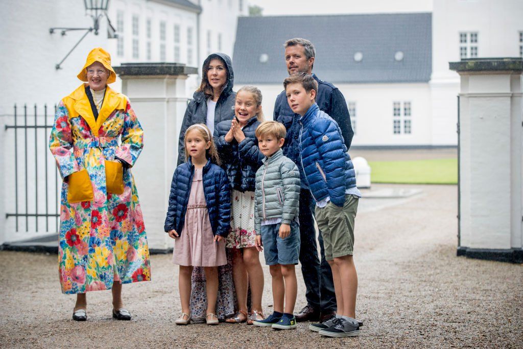 Queen Margrethe, wearing a very colourful and flamboyant floral and yellow anorak pictured with her son Crown Prince Frederik of Denmark and other family members - who are wearing more usual rainy summer clothes